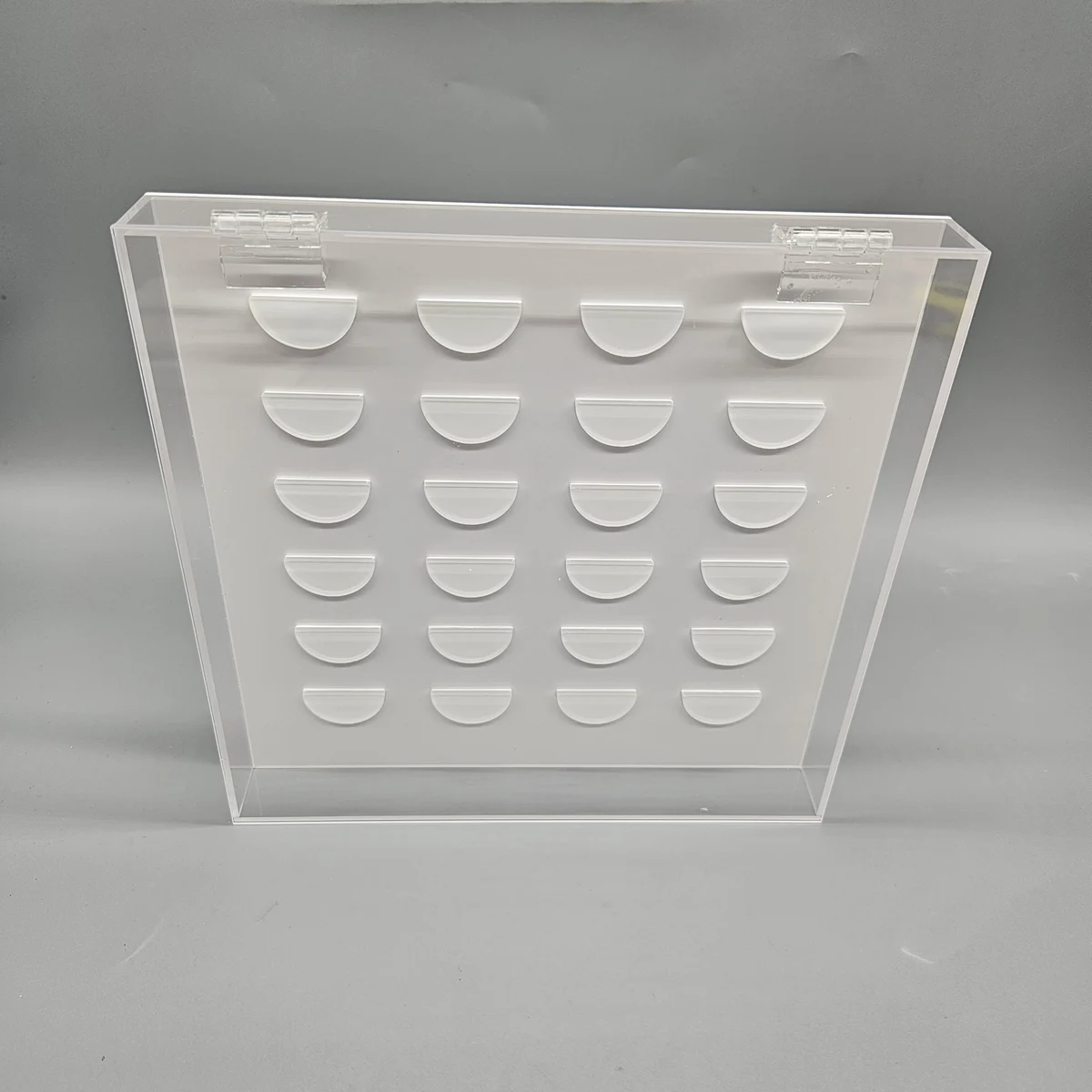 Original archive reference: Clear hinged acrylic false lash display case with 24 semicircular holders on a white insert